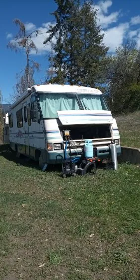 Vintage motorhome RV with mobile A/C service setup beside it — vacuum pump and refrigerant cylinder staged
